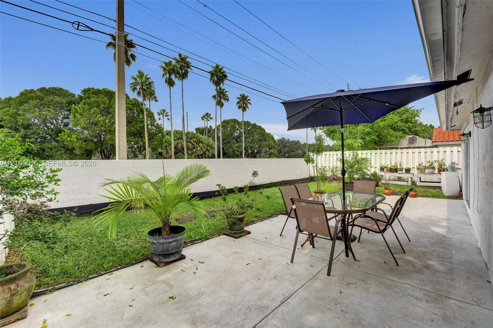 631 NW 135th Terrace, Plantation, FL 33325 Concrete patio area featuring a low-maintenance lawn, white perimeter wall, and exterior wall-mounted light fixtures