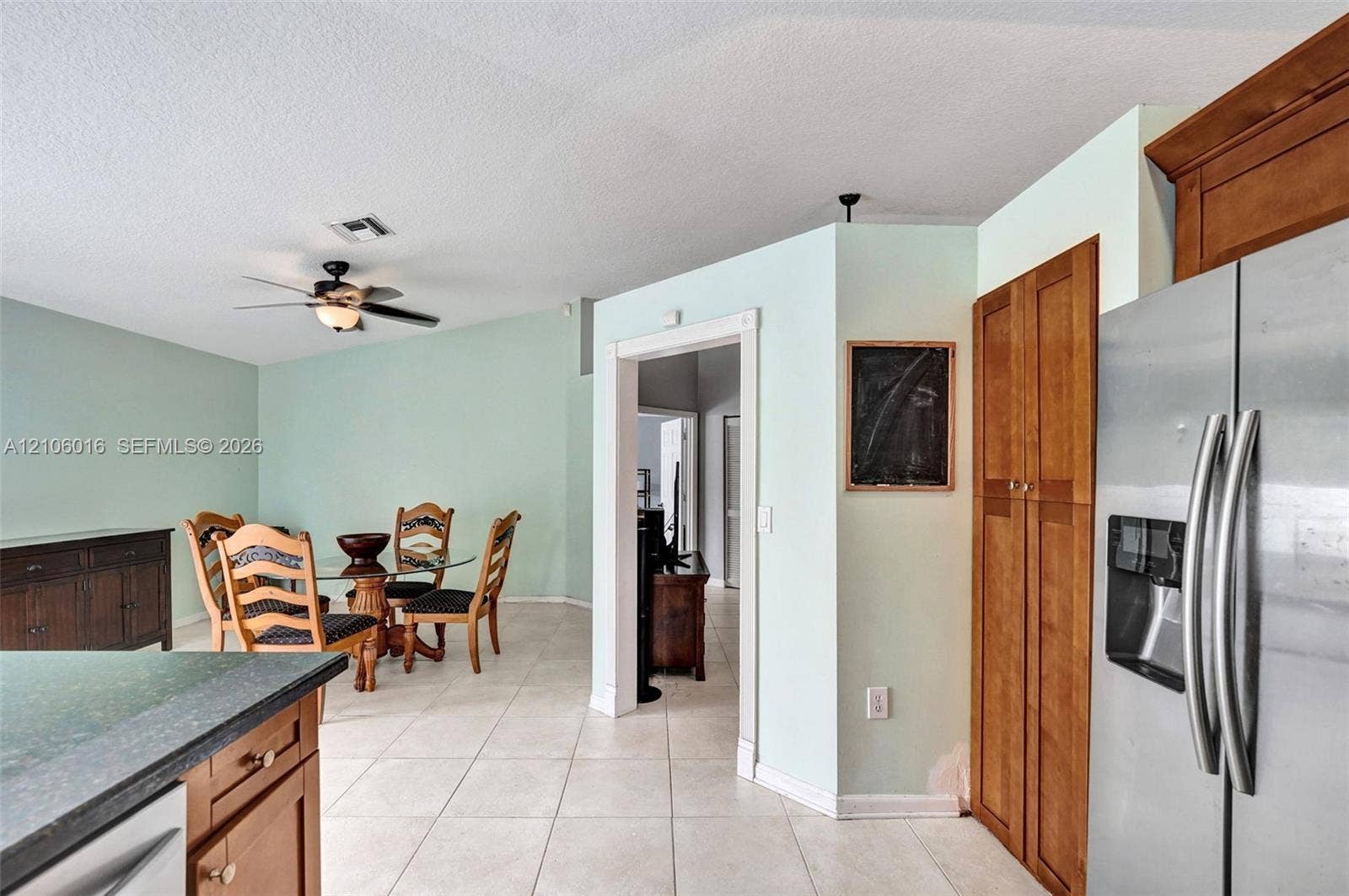 631 NW 135th Terrace, Plantation, FL 33325 Kitchen and dining area featuring wood cabinetry, tile flooring, a stainless steel refrigerator, and a ceiling fan with light fixture