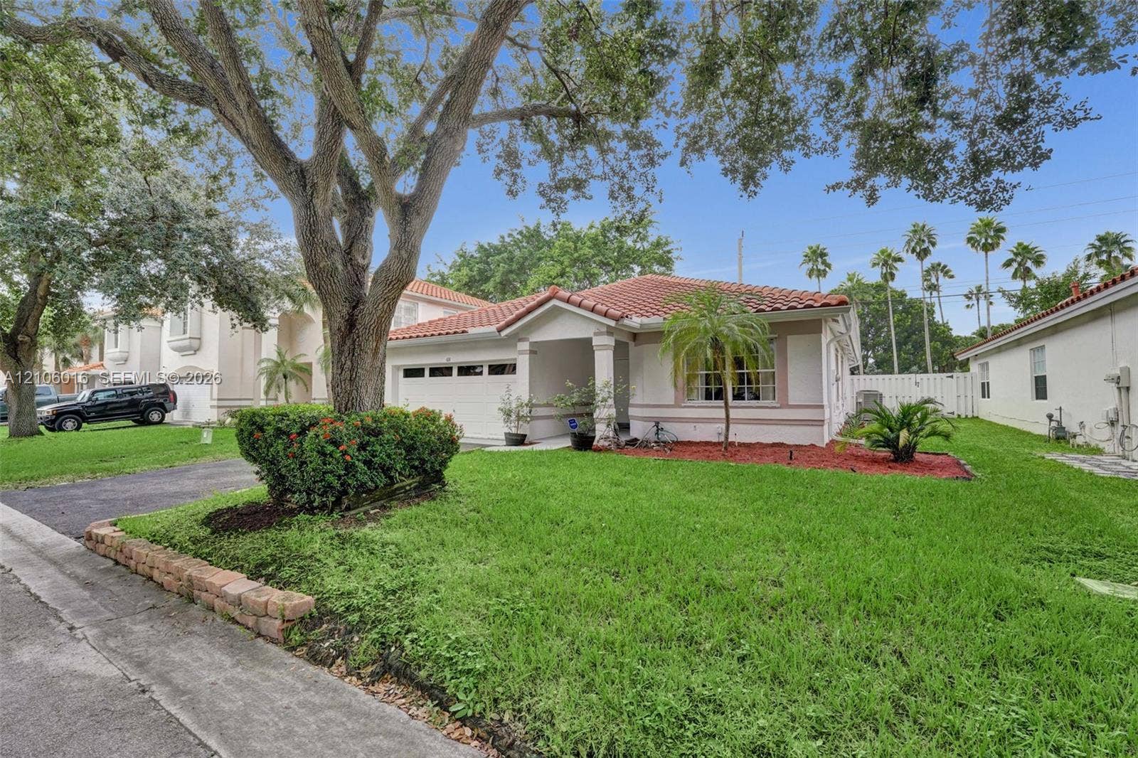 631 NW 135th Terrace, Plantation, FL 33325 Single-story residence featuring a terracotta-tile roof, stucco exterior, integrated garage, concrete paver-style edging, and mature landscaping