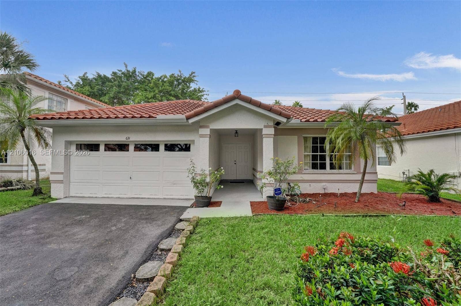 631 NW 135th Terrace, Plantation, FL 33325 Stucco exterior featuring a tiled roof, covered entryway, multi-panel garage door, and defined landscape beds
