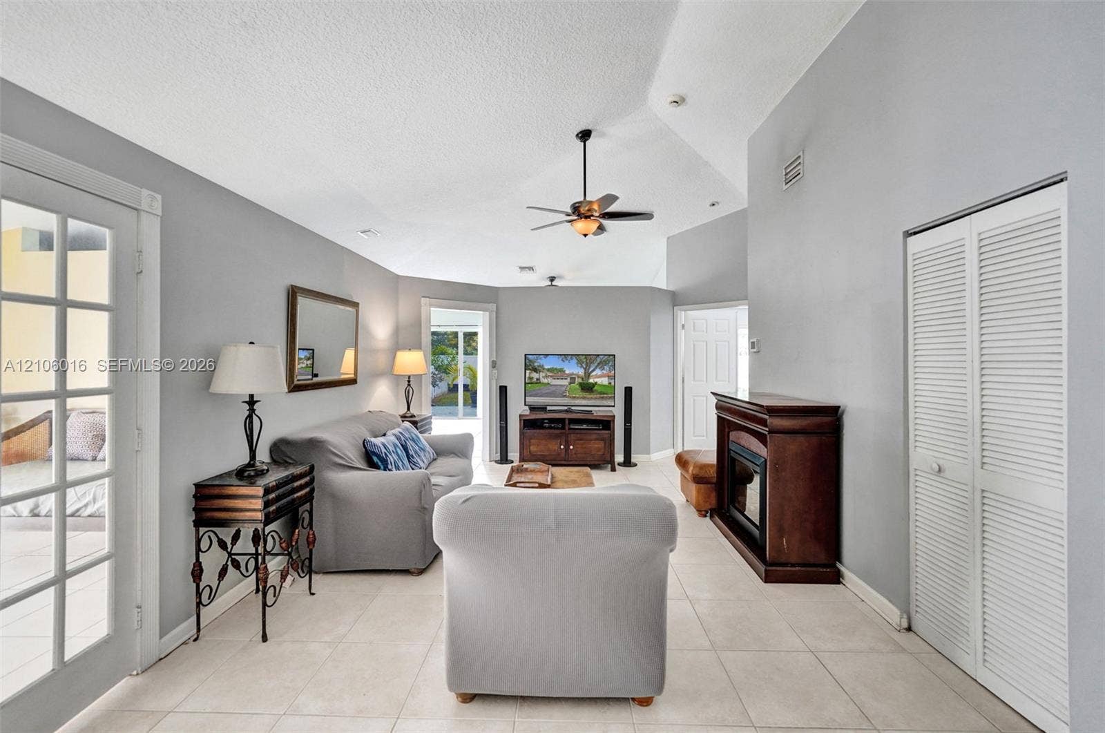 631 NW 135th Terrace, Plantation, FL 33325 Living area featuring vaulted ceilings, large-format tile flooring, a fireplace with a wood-finish mantel, louvered closet doors, and glass-paned double doors