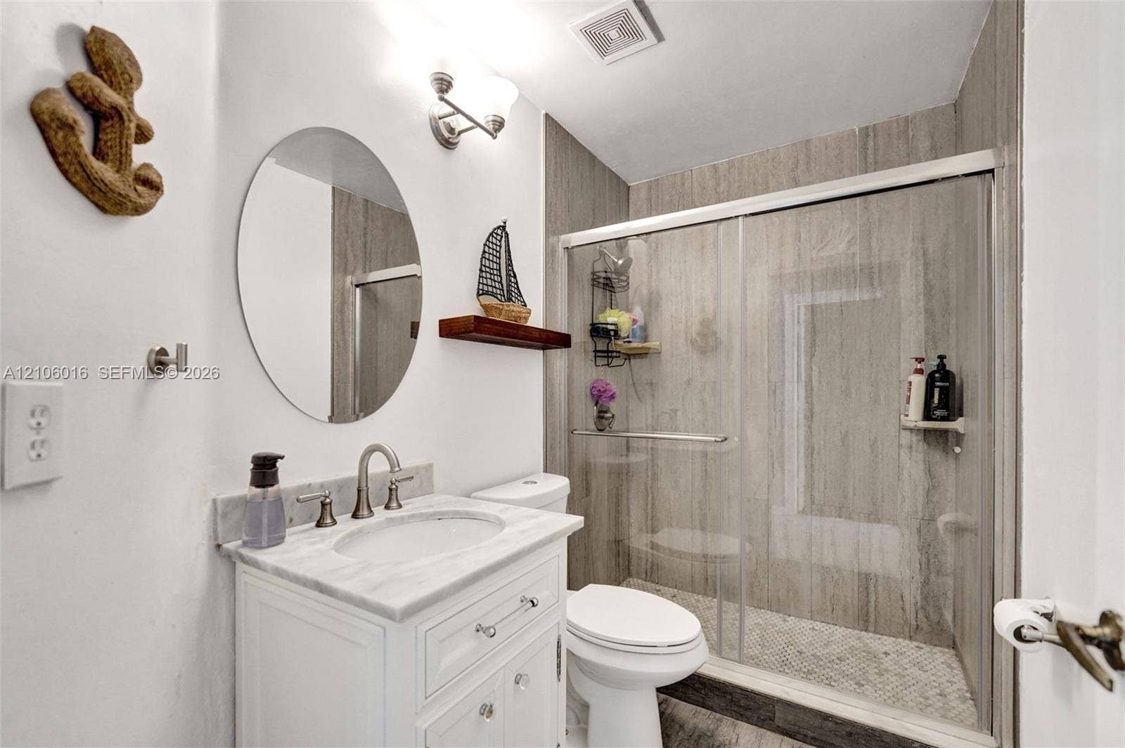 631 NW 135th Terrace, Plantation, FL 33325 Bathroom featuring a white vanity with a stone countertop, an oval wall-mounted mirror, and a walk-in shower with sliding glass doors and large-format tile surround