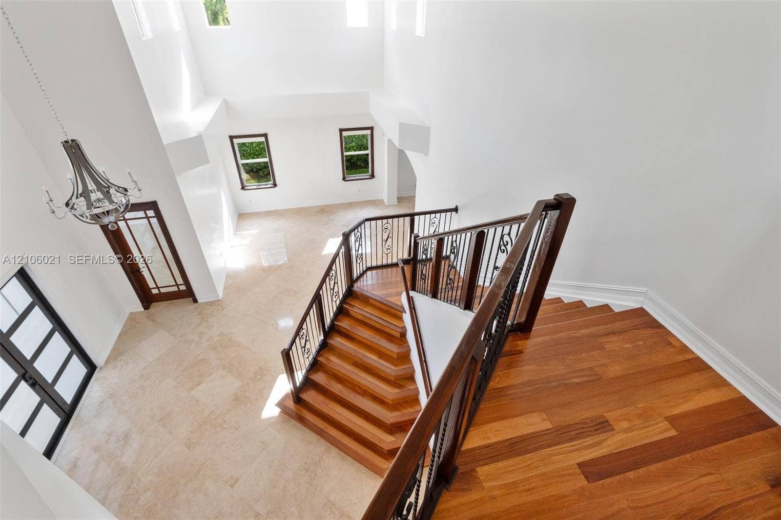 19510 S Coquina Way, Weston, FL 33332 Open-concept entry featuring soaring ceilings, wood-finish staircase with wrought-iron balusters, neutral stone-tile flooring, and multiple high-reach windows