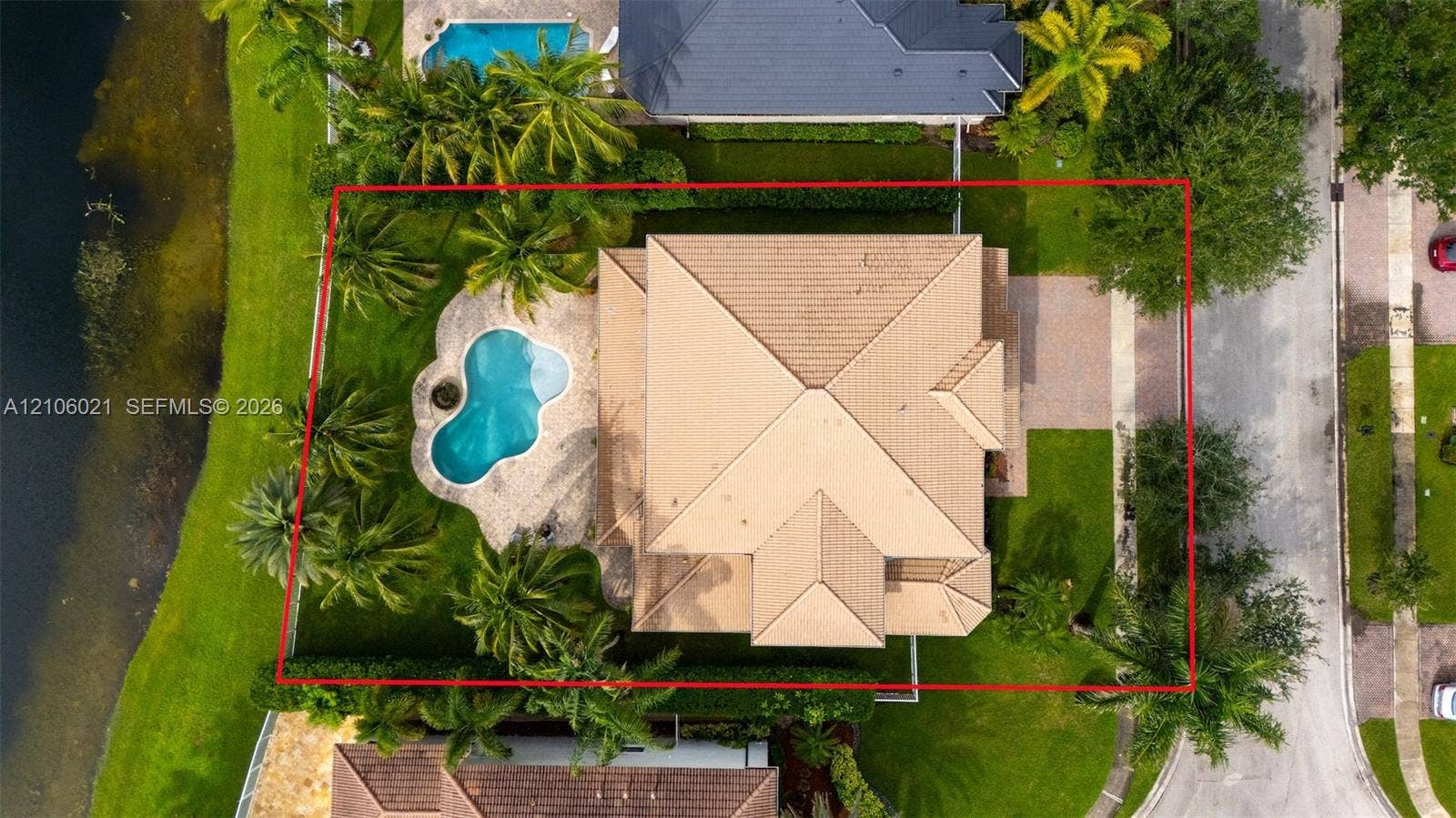 19510 S Coquina Way, Weston, FL 33332 Aerial perspective of a property featuring a tile roof, an in-ground swimming pool, a paved patio, and mature palm trees situated on a waterfront lot