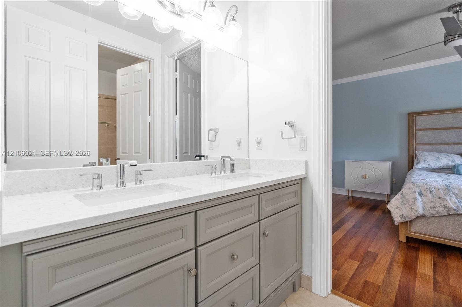 19510 S Coquina Way, Weston, FL 33332 Double vanity featuring gray shaker-style cabinetry, a light-toned solid surface countertop, dual undermount sinks, and polished chrome faucets, finished with a multi-bulb vanity light fixture