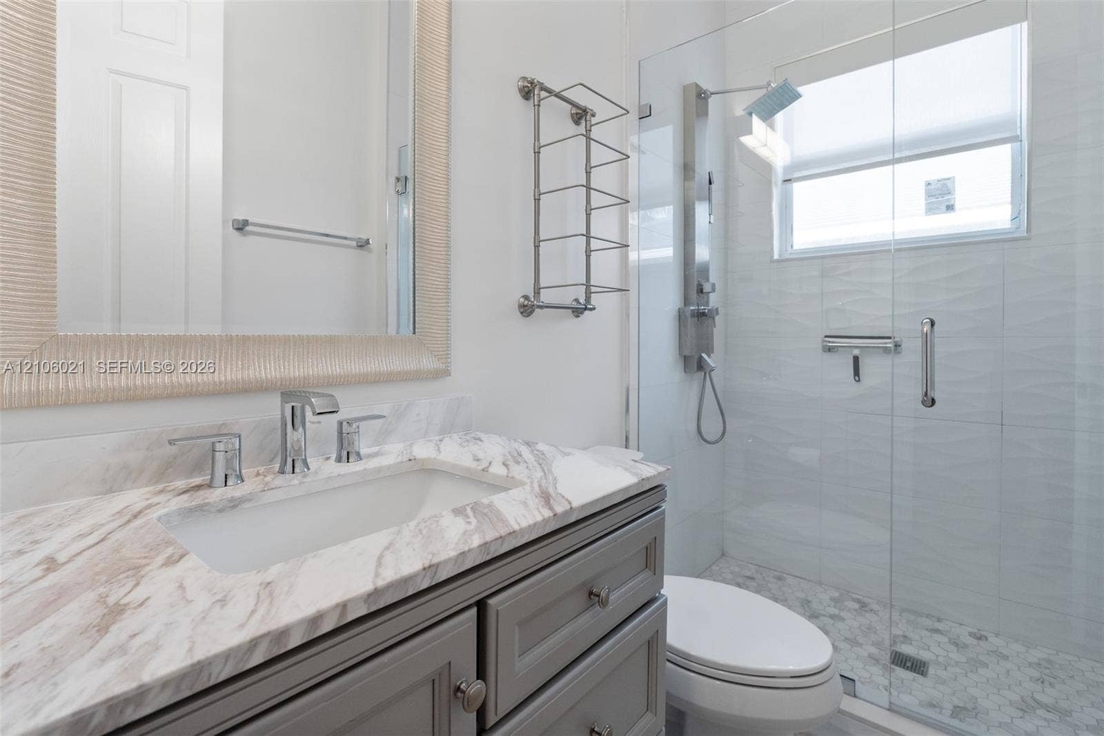 19510 S Coquina Way, Weston, FL 33332 Grey shaker-style vanity with a stone countertop, integrated sink, chrome-finish faucet, and glass-enclosed shower featuring a rainfall showerhead and pebble-tile floor