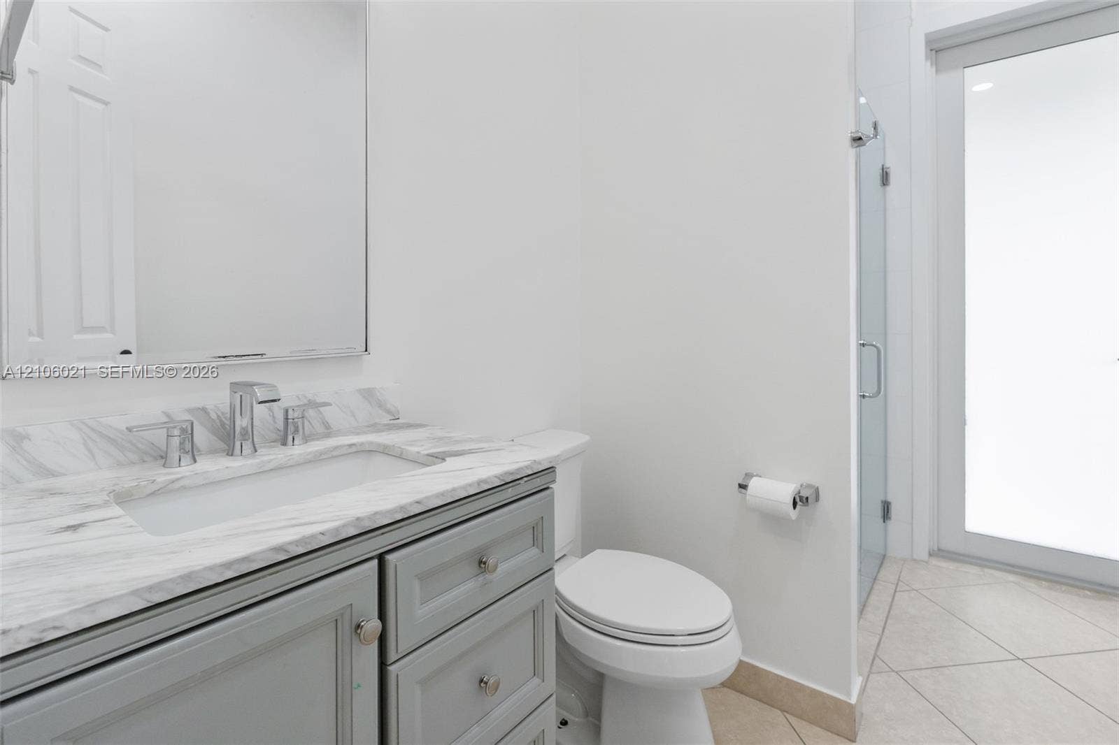 19510 S Coquina Way, Weston, FL 33332 Vanity with a neutral-toned countertop and integrated basin, frameless wall-mounted mirror, cabinetry with brushed hardware, and glass-enclosed shower with tile flooring