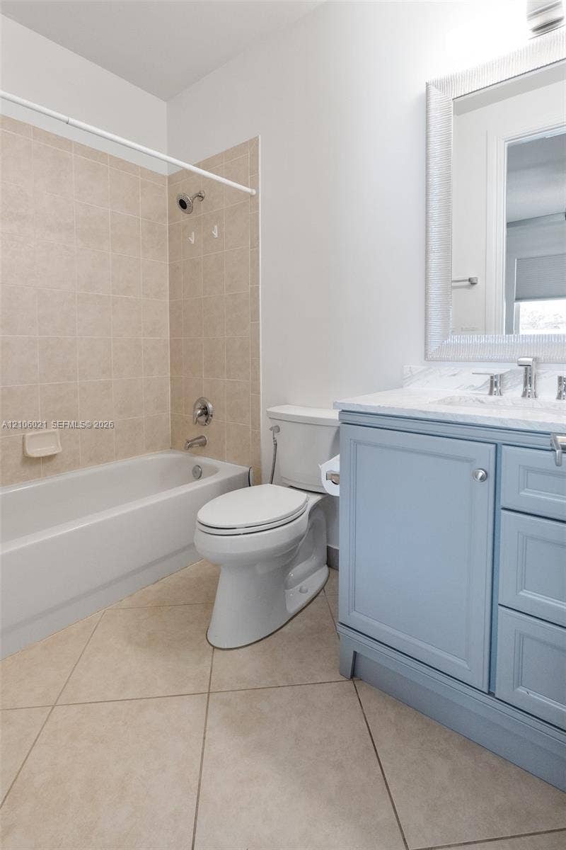 19510 S Coquina Way, Weston, FL 33332 Bathroom featuring a light blue vanity with a stone countertop, an integrated porcelain sink, a bathtub with beige tiled surround, and ceramic tile flooring