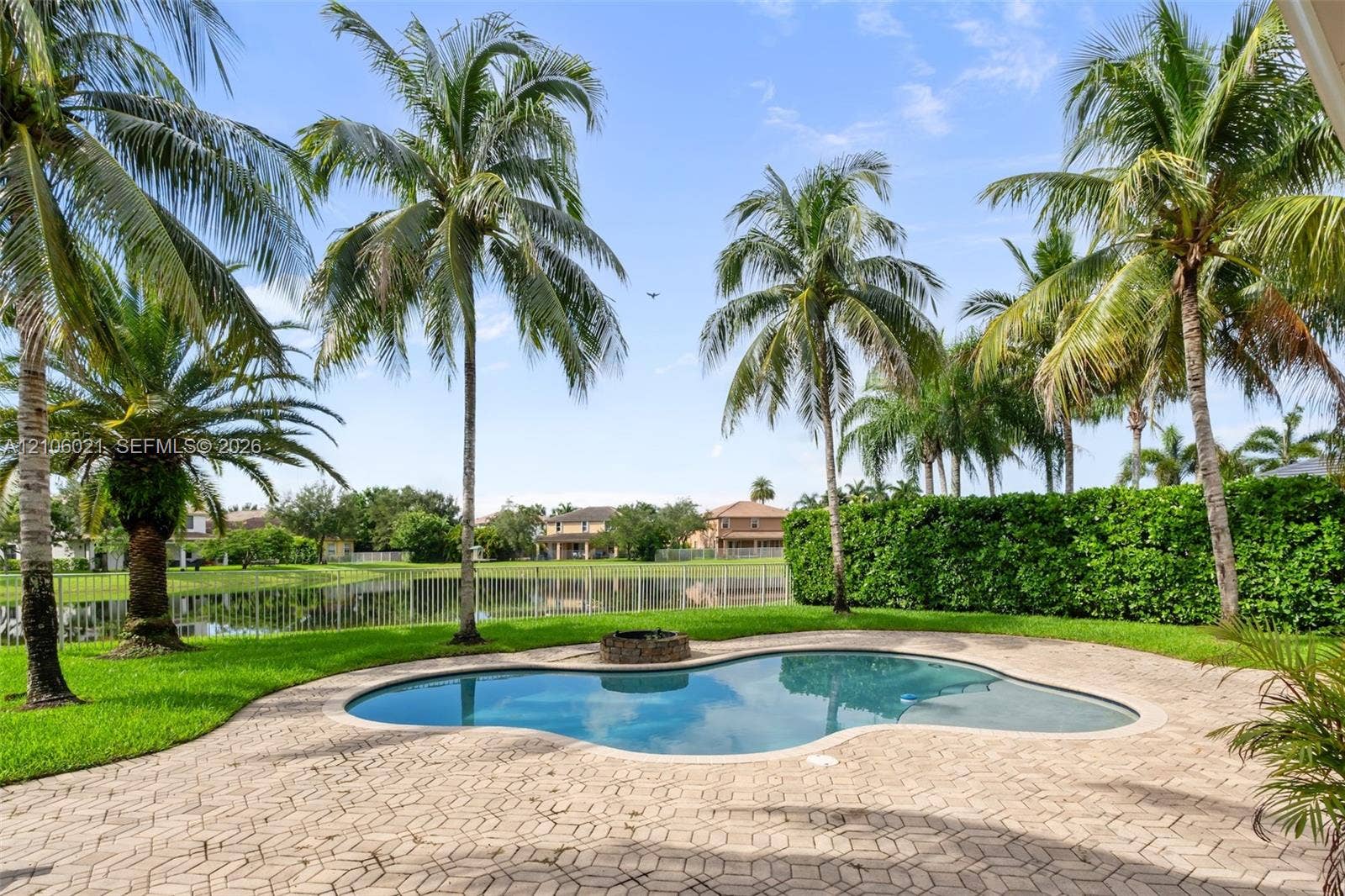 19510 S Coquina Way, Weston, FL 33332 Free-form swimming pool with stone-accented fire pit, paver patio, mature palm trees, and waterfront perimeter fencing