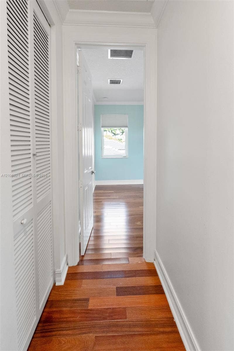19510 S Coquina Way, Weston, FL 33332 Hallway featuring wood-finish flooring, white louvered-style closet doors, crown molding, and a paneled interior door leading to a room with light-toned wall finishes