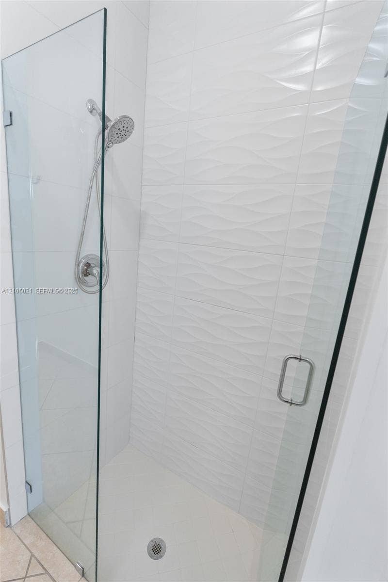 19510 S Coquina Way, Weston, FL 33332 Walk-in shower enclosure featuring frameless glass doors, white textured wall tile, chrome shower hardware, and a built-in shower head