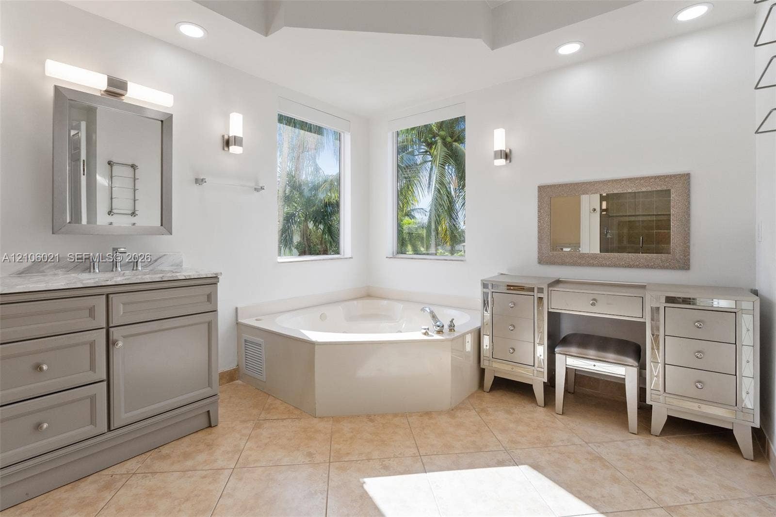 19510 S Coquina Way, Weston, FL 33332 Bathroom featuring a corner jetted soaking tub, custom grey cabinetry with stone-finish countertop, dual wall-mounted light fixtures, and tiled flooring
