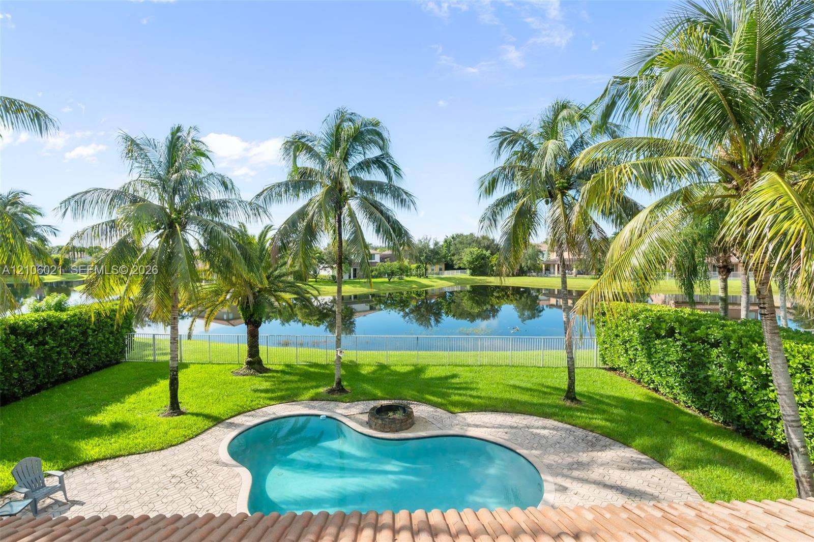 19510 S Coquina Way, Weston, FL 33332 Backyard featuring a freeform swimming pool, stone paver decking, integrated stone fire pit, manicured lawn, and mature palm trees