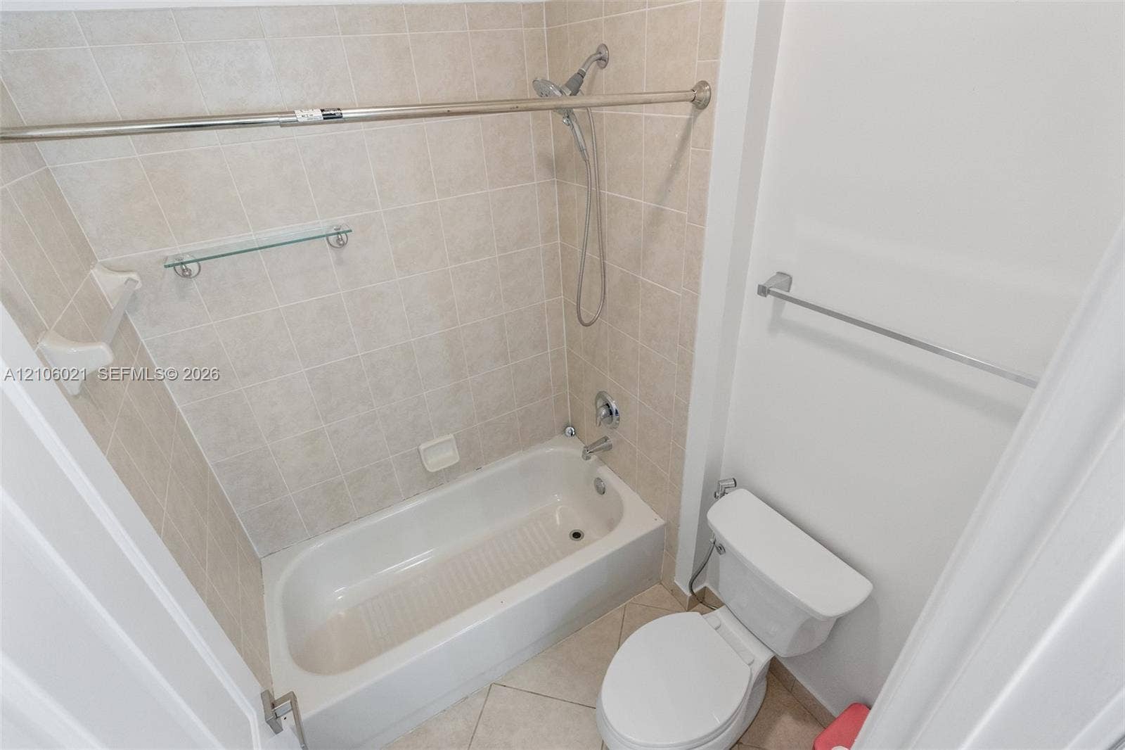 19510 S Coquina Way, Weston, FL 33332 Full bathroom featuring a porcelain bathtub with a showerhead attachment, neutral tile surround, integrated glass shelf, and a ceramic toilet