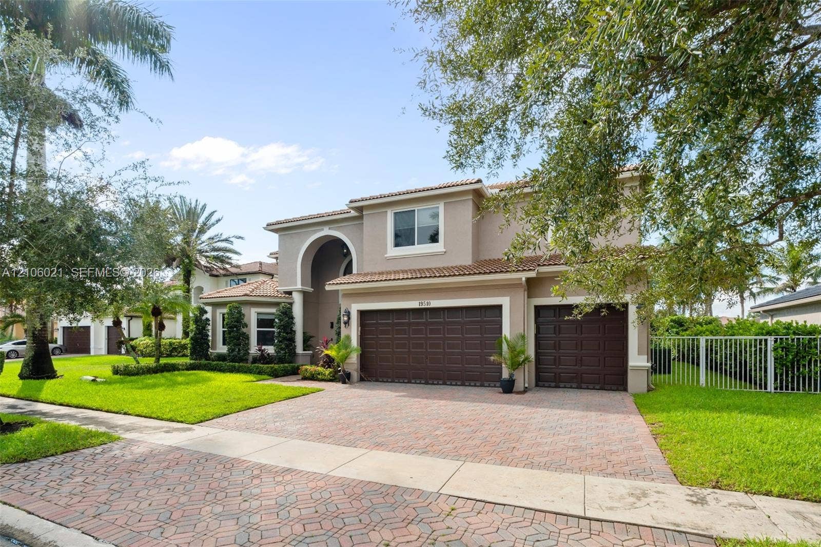 19510 S Coquina Way, Weston, FL 33332 Two-story residence featuring a terracotta-tiled roof, an arched entryway, a three-car garage with dark paneled doors, and a decorative brick-paver driveway