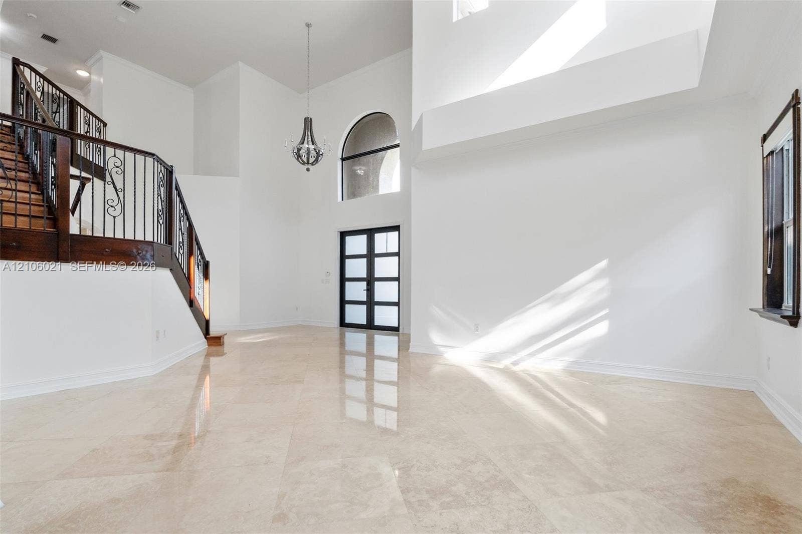19510 S Coquina Way, Weston, FL 33332 Double-height foyer with stone tile flooring, iron balustrade staircase, multi-lite glass panel front door, arched window, and tiered pendant chandelier