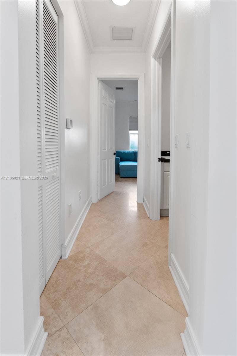 19510 S Coquina Way, Weston, FL 33332 Interior hallway featuring diagonal-patterned stone flooring, louvered closet doors, and crown molding