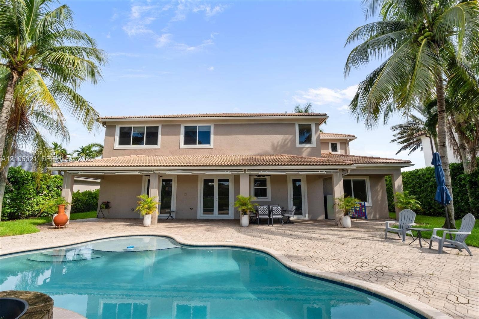 19510 S Coquina Way, Weston, FL 33332 Two-story exterior featuring a tile roof, covered rear patio, expansive paver pool deck, free-form swimming pool, and mature palm trees