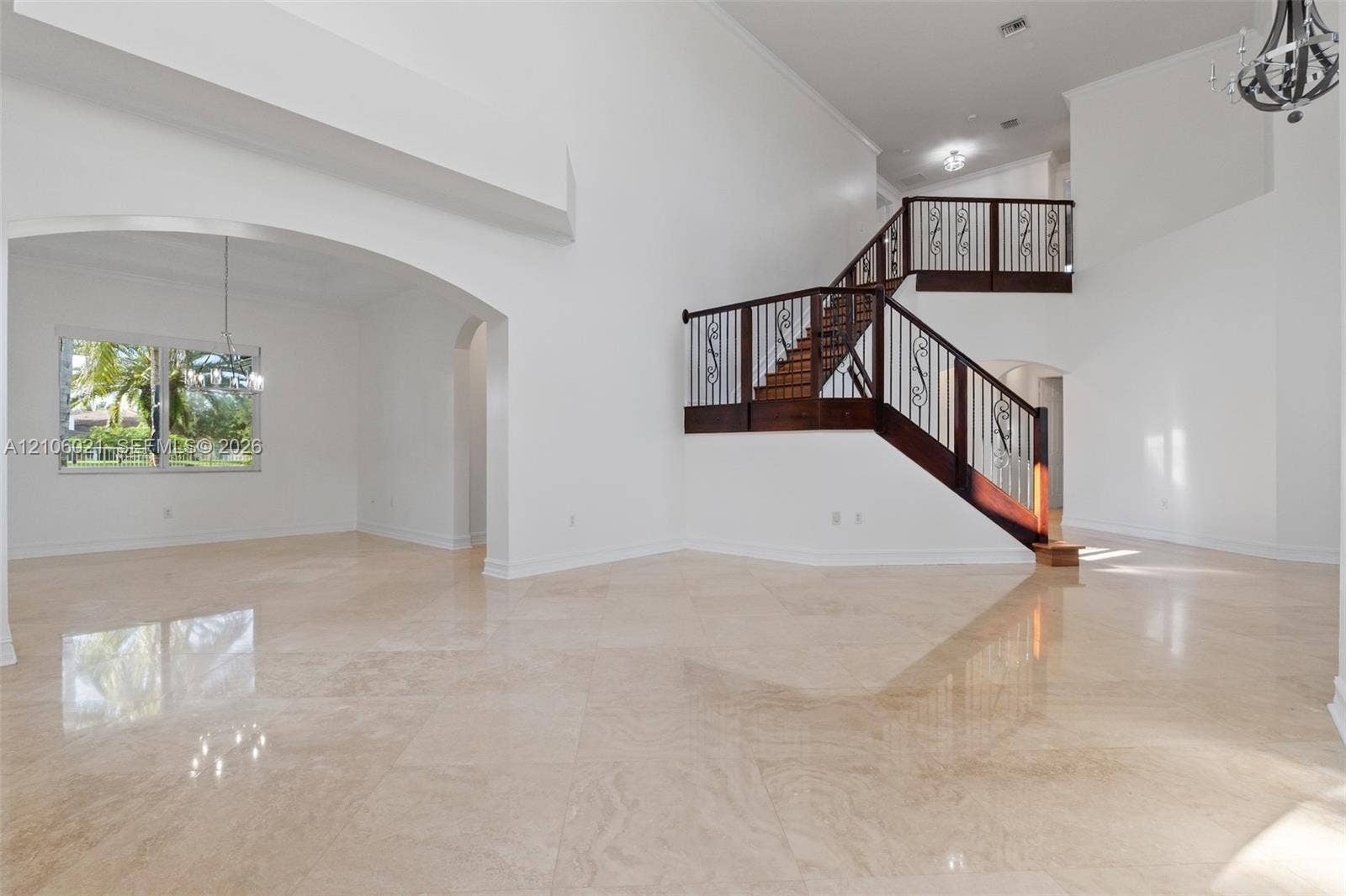 19510 S Coquina Way, Weston, FL 33332 High-ceilinged interior featuring polished stone flooring, a staircase with wood railings and decorative metal balusters, and arched architectural detailing