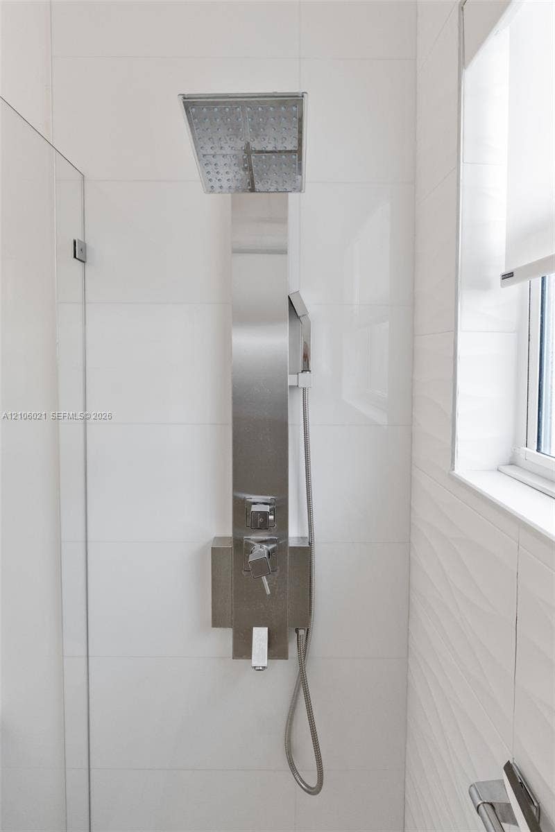 19510 S Coquina Way, Weston, FL 33332 Shower enclosure featuring a stainless steel rainfall shower panel with a hand-held sprayer, smooth white tile walls, and a textured white accent wall