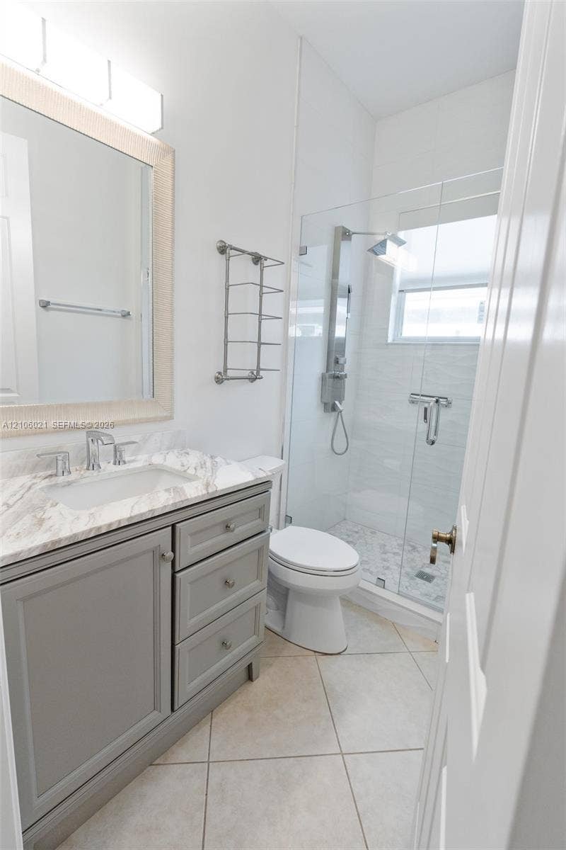 19510 S Coquina Way, Weston, FL 33332 Bathroom featuring a stone-finish vanity top, grey shaker-style cabinetry, a glass-enclosed shower with a rainfall showerhead, and ceramic tile flooring