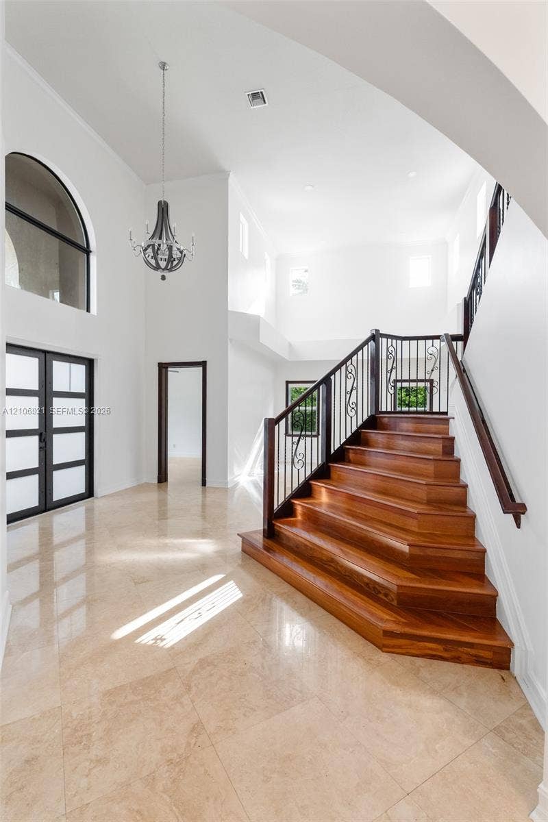 19510 S Coquina Way, Weston, FL 33332 Grand foyer featuring stone flooring, a soaring vaulted ceiling, a statement chandelier, multi-pane glass entry doors, and a staircase with wood treads and ornate metal railings
