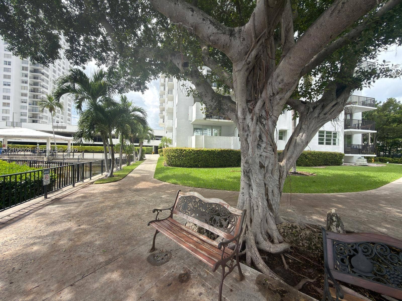 2780 NE 183rd Street, #1605, Aventura, FL 33160 Landscaped grounds featuring mature trees, manicured hedges, paved walking paths, and metal perimeter fencing