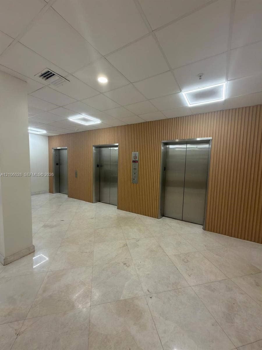 2780 NE 183rd Street, #1605, Aventura, FL 33160 Elevator lobby featuring three stainless steel elevator doors, ribbed wood-panel wall cladding, polished stone flooring, and recessed LED ceiling panels