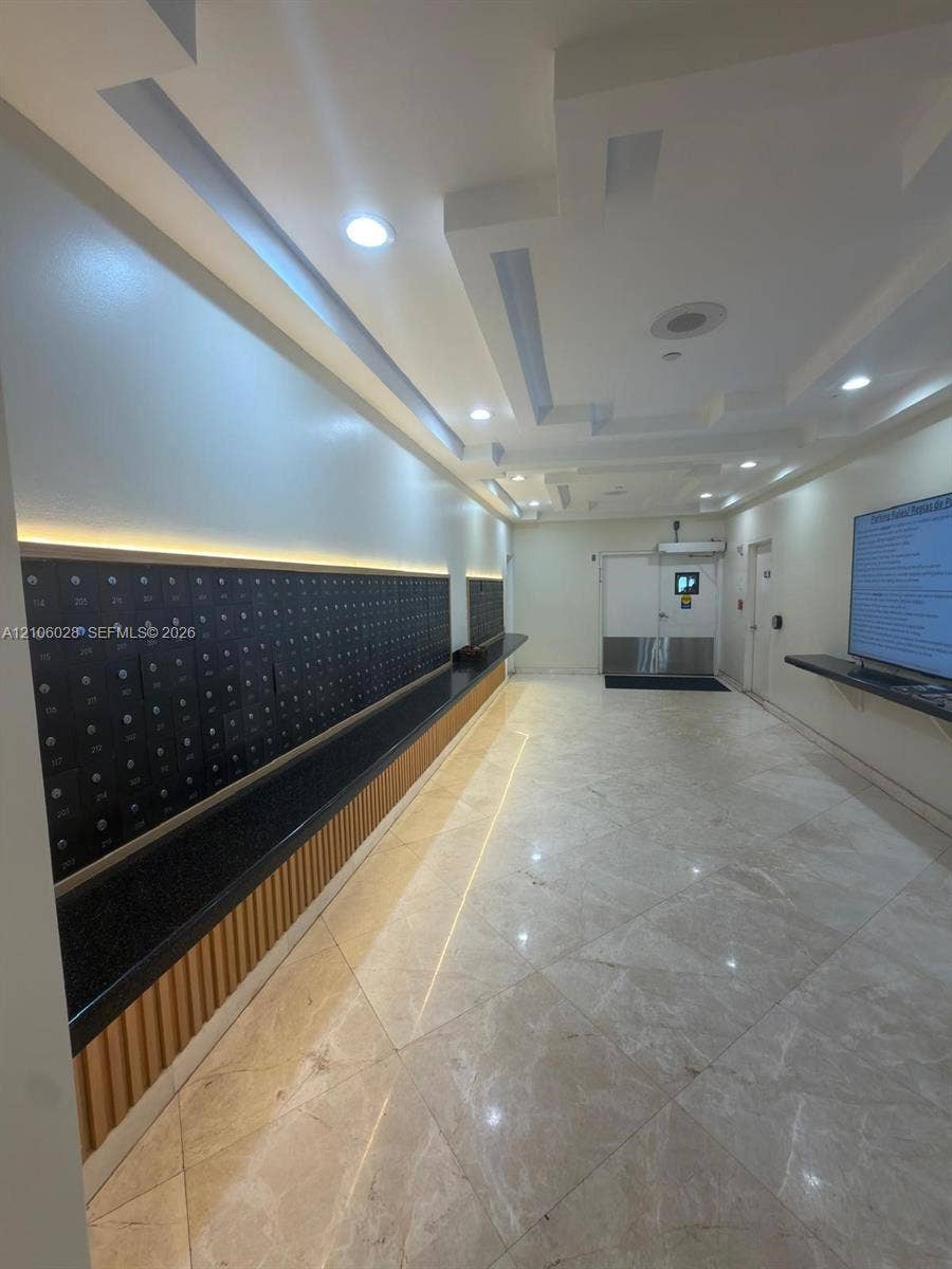2780 NE 183rd Street, #1605, Aventura, FL 33160 Communal mail area featuring stone tile flooring, recessed coffered ceilings with integrated lighting, wall-mounted mailboxes with a stone-finish counter, and vertical wood-slat accent detailing