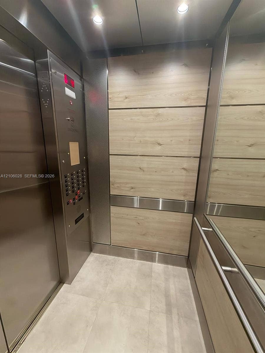2780 NE 183rd Street, #1605, Aventura, FL 33160 Elevator cab featuring wood-finish paneling, stainless steel trim, integrated mirror, brushed metal control panel, and recessed ceiling lighting