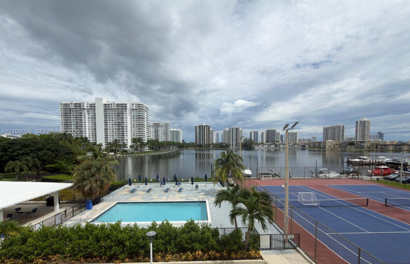 2780 NE 183rd Street, #1605, Aventura, FL 33160 Community recreational area featuring a swimming pool, hard-court tennis facilities, and landscaped palm trees, positioned alongside a waterfront with boat docking