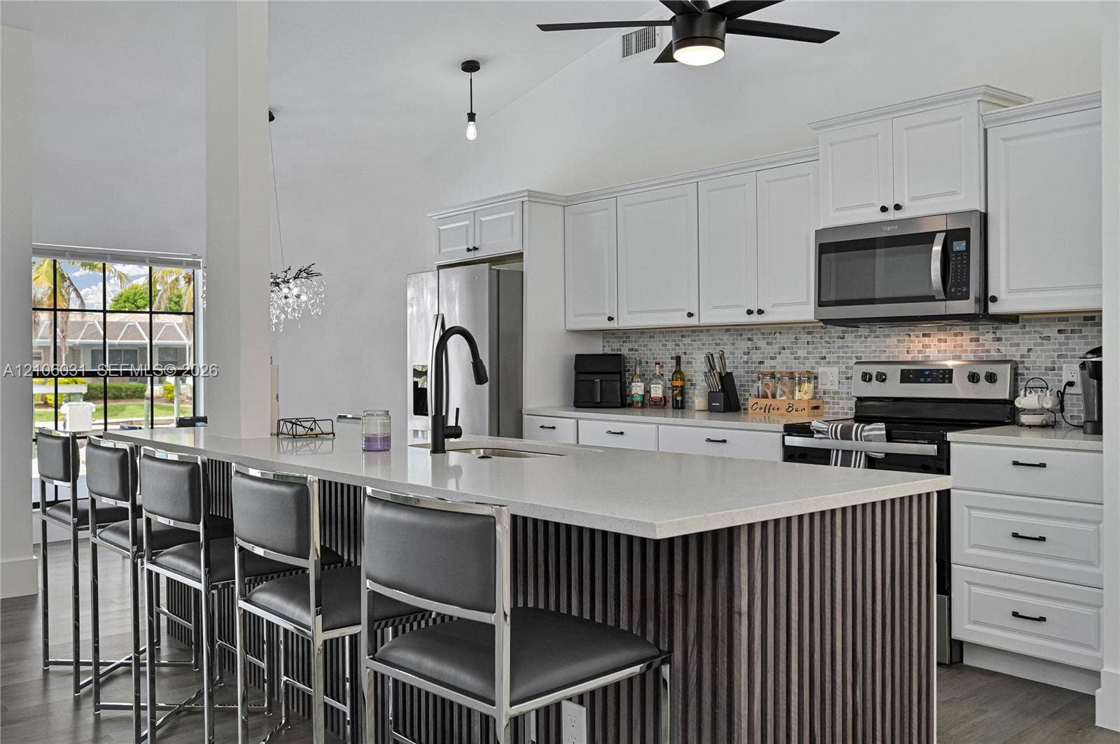 1106 SE 23rd Place, Cape Coral, FL 33990 Kitchen featuring white shaker-style cabinetry, quartz countertops, a slatted wood-finish kitchen island, a mosaic tile backsplash, and stainless steel appliances