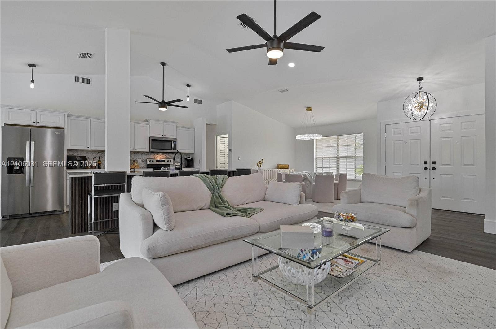 1106 SE 23rd Place, Cape Coral, FL 33990 Open-concept interior featuring vaulted ceilings, wood-finish flooring, white shaker cabinetry, stainless steel kitchen appliances, and contemporary multi-arm chandeliers