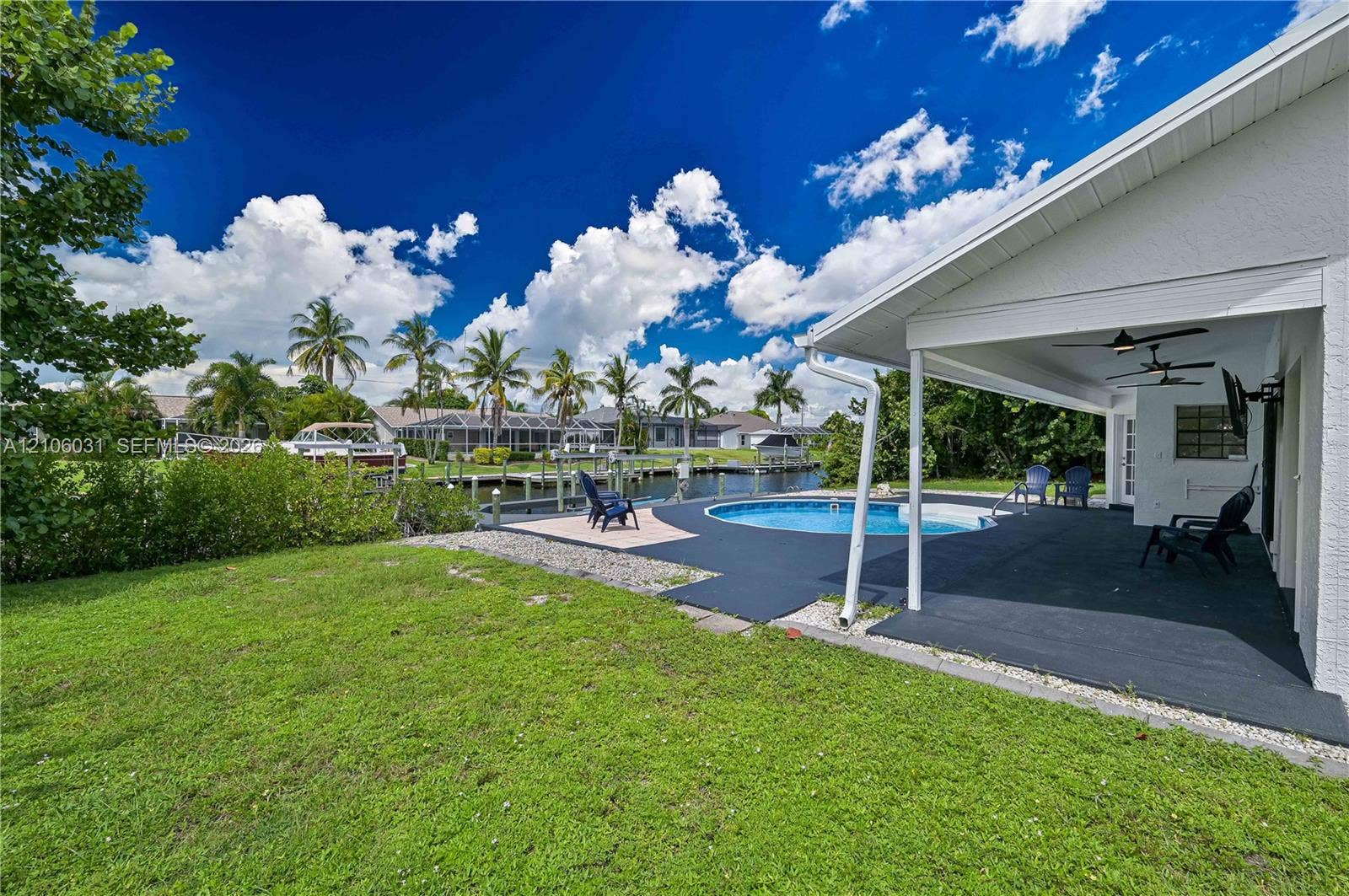 1106 SE 23rd Place, Cape Coral, FL 33990 Covered patio featuring two ceiling fans, in-ground swimming pool, concrete pool deck, and private boat dock situated on a canal