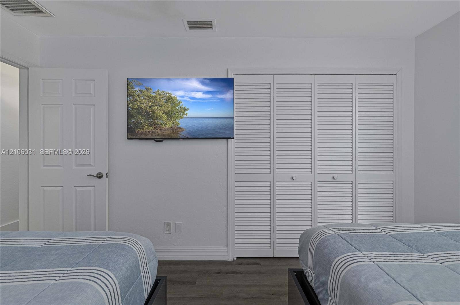 1106 SE 23rd Place, Cape Coral, FL 33990 Room featuring wood-finish flooring, white louvered-style closet doors, and a solid-panel interior door with a brushed nickel lever handle
