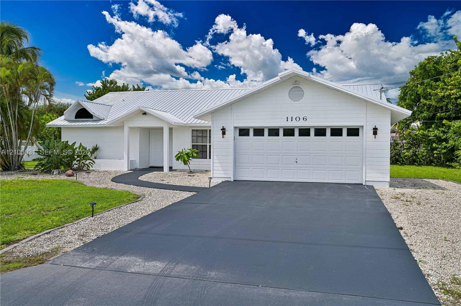 1106 SE 23rd Place, Cape Coral, FL 33990 White exterior residence featuring a standing seam metal roof, attached two-car garage with glass-paneled door, and paved driveway