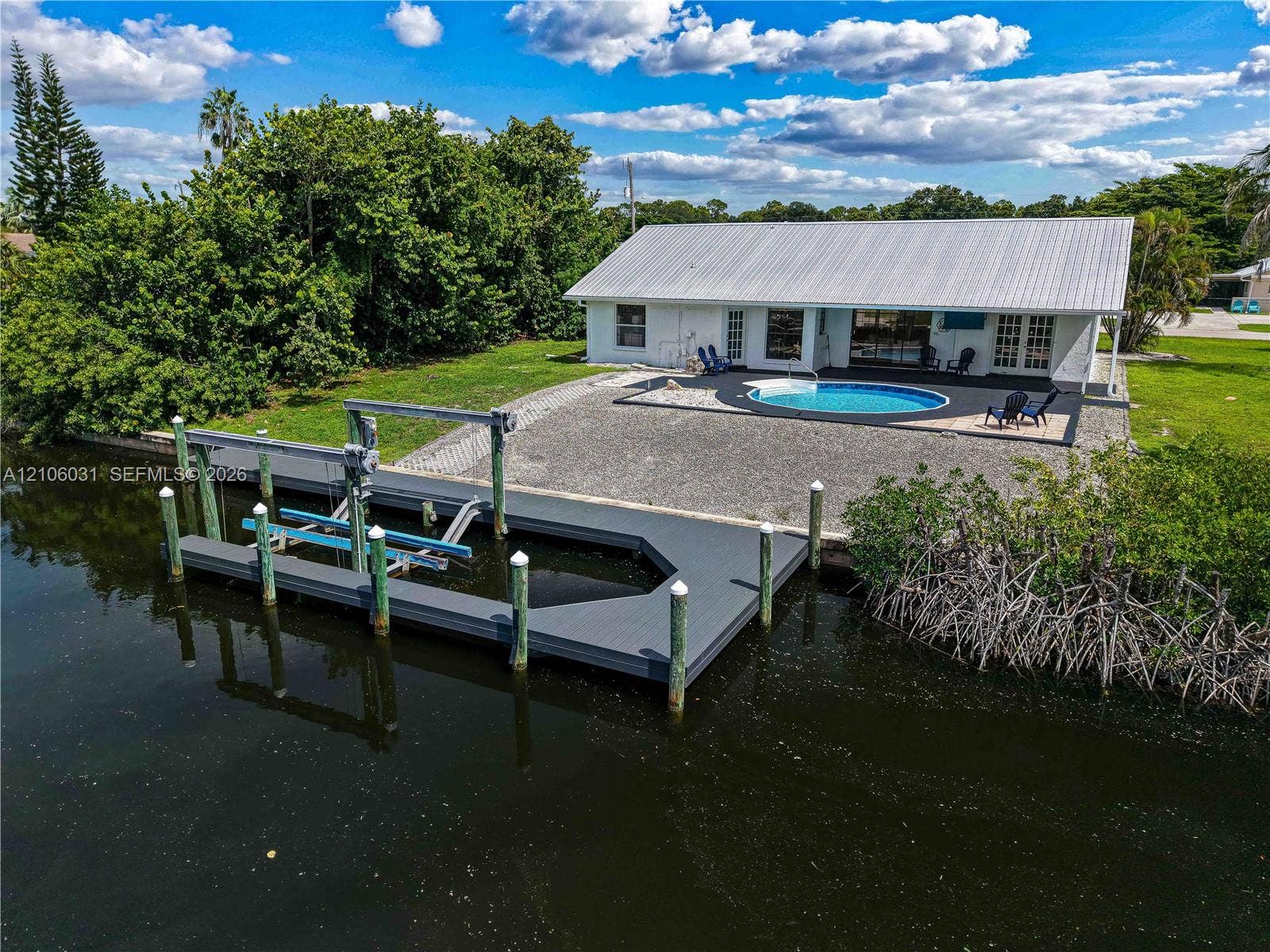 1106 SE 23rd Place, Cape Coral, FL 33990 Waterfront property featuring a private boat dock with a mechanical lift, an in-ground swimming pool, a metal roof, and stone-surfaced patio area