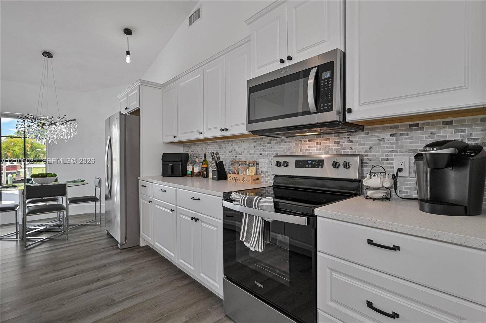 1106 SE 23rd Place, Cape Coral, FL 33990 Kitchen featuring white Shaker-style cabinetry, stainless steel appliances, a mosaic tile backsplash, quartz countertops, and wood-finish flooring