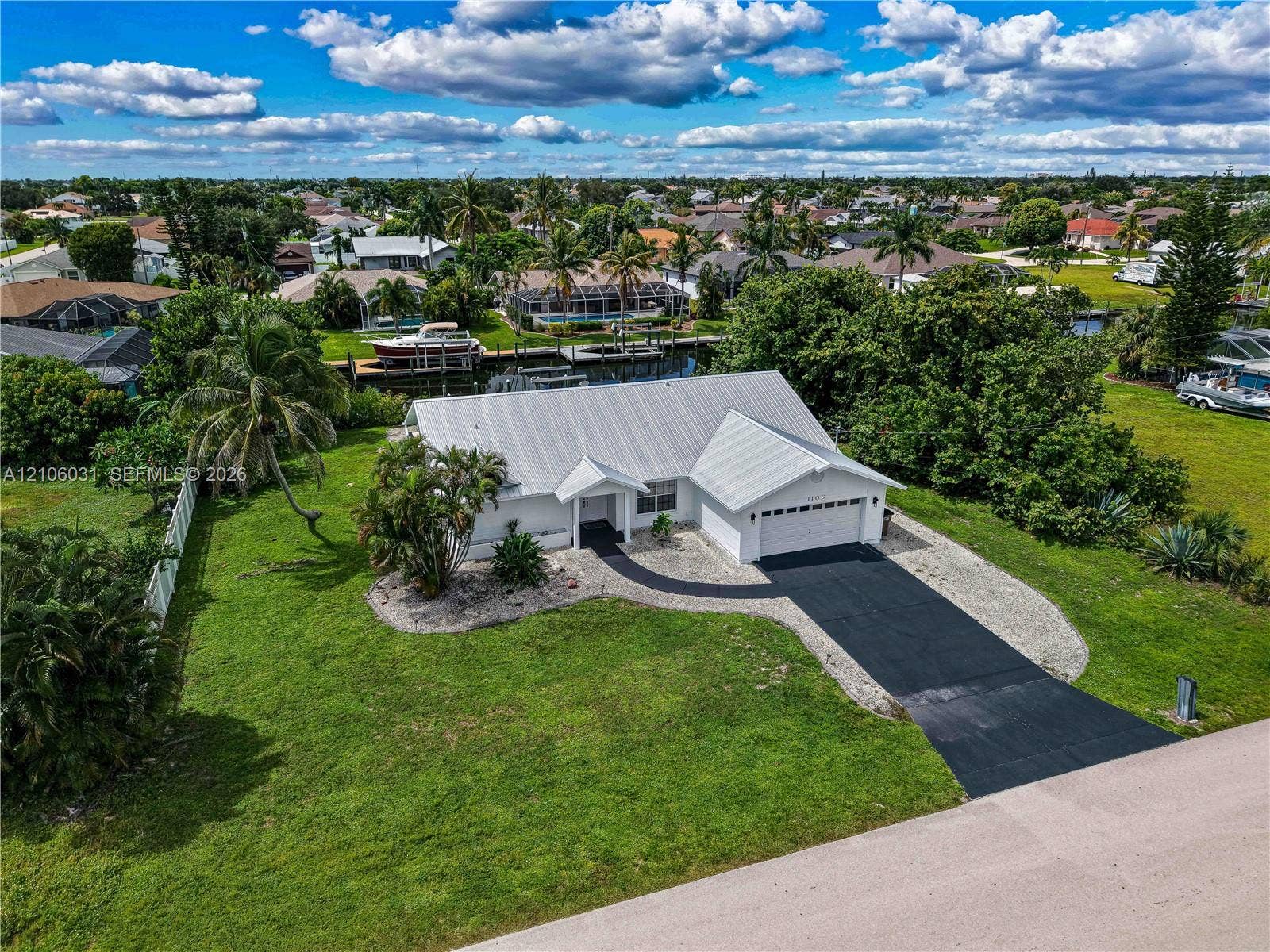 1106 SE 23rd Place, Cape Coral, FL 33990 Waterfront property featuring a metal roof, attached two-car garage, paved driveway, and expansive lawn area