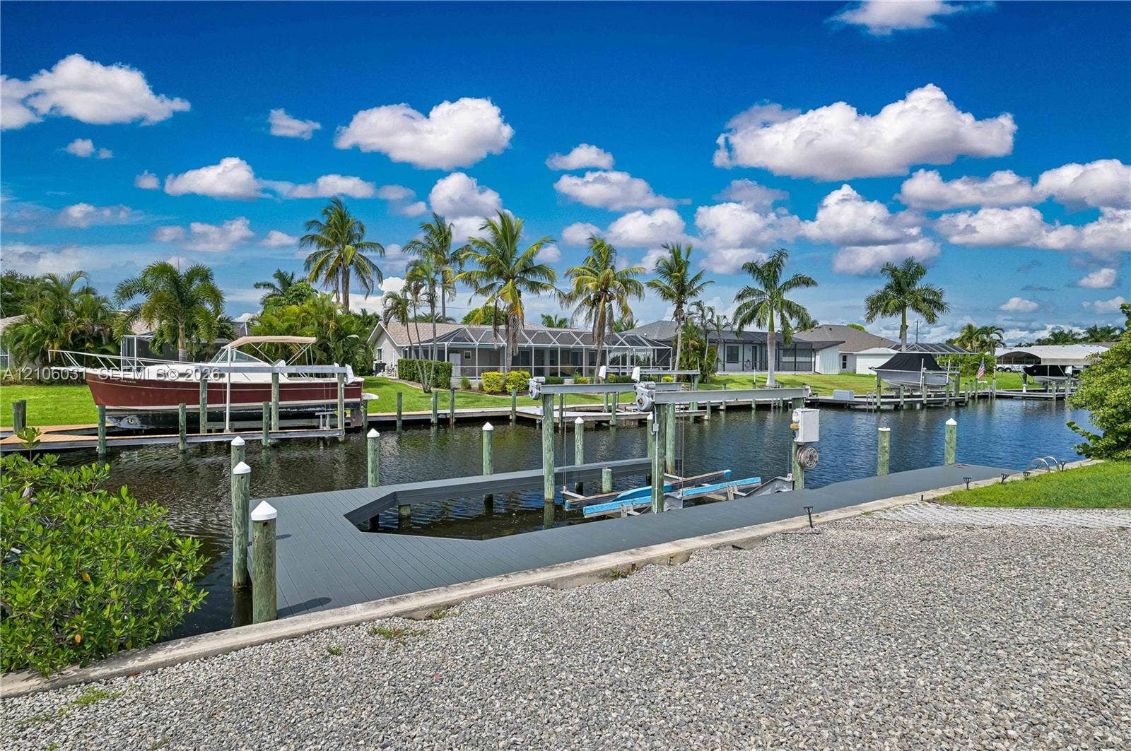 1106 SE 23rd Place, Cape Coral, FL 33990 Waterfront estate featuring a pristine boat dock with direct water access, mature palm trees throughout the manicured grounds, expansive green lawn, and multiple residential structures with covered boat slips and mooring posts along the canal frontage