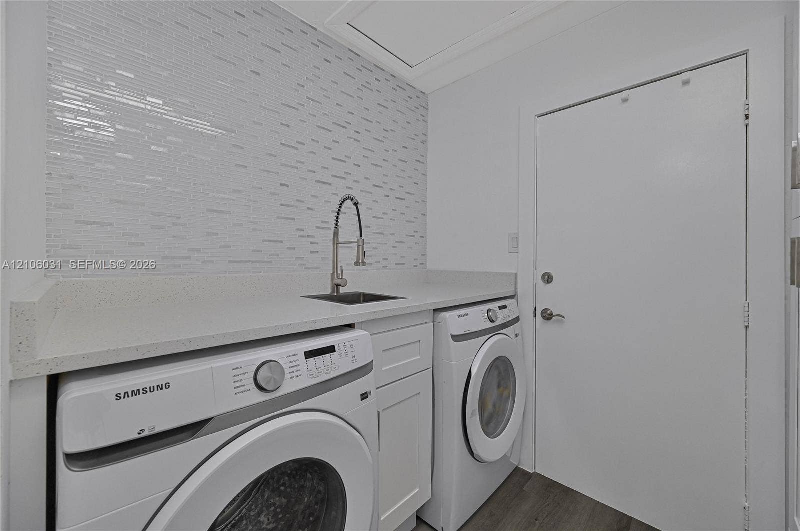 1106 SE 23rd Place, Cape Coral, FL 33990 Laundry area featuring a stone countertop, an integrated sink with a gooseneck faucet, a textured tile backsplash, white shaker-style cabinetry, and wood-finish flooring