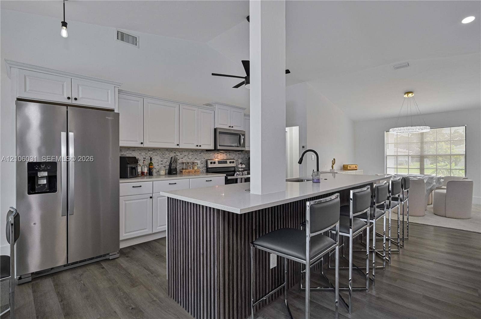 1106 SE 23rd Place, Cape Coral, FL 33990 Kitchen featuring white cabinetry, wood-finish flooring, a central island with a slatted wood base and quartz countertop, stainless steel appliances, and a mosaic tile backsplash