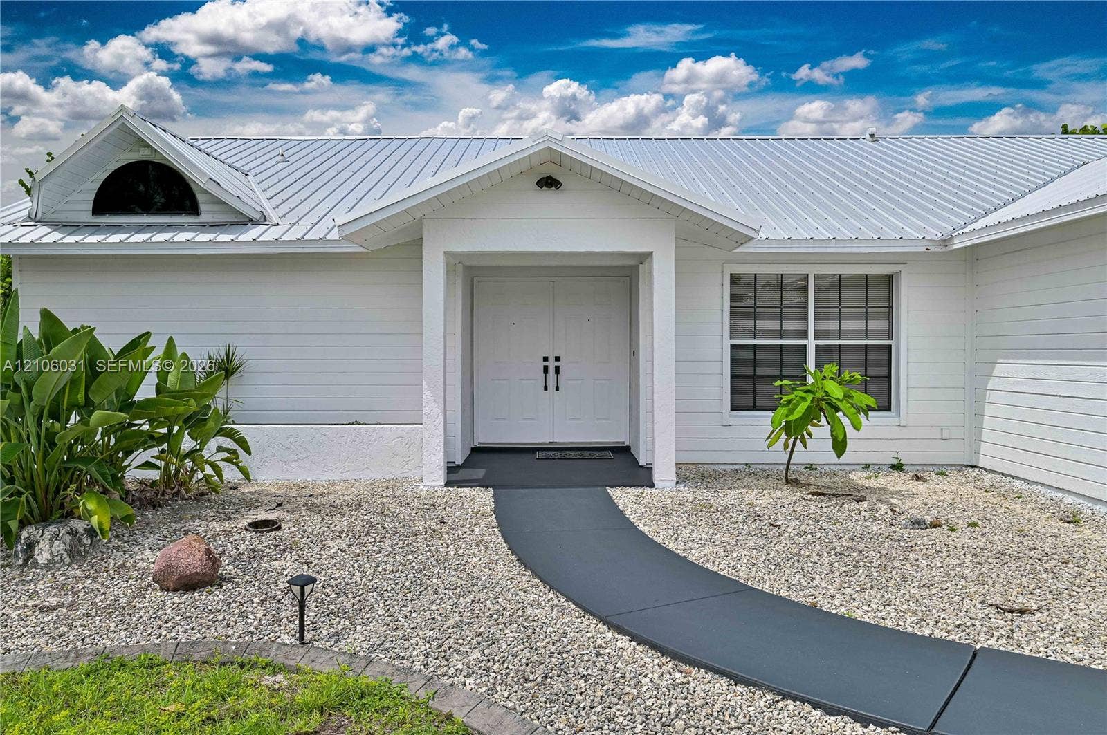1106 SE 23rd Place, Cape Coral, FL 33990 Exterior facade featuring white horizontal siding, a metal roof, a semi-circular accent window, and double entry doors