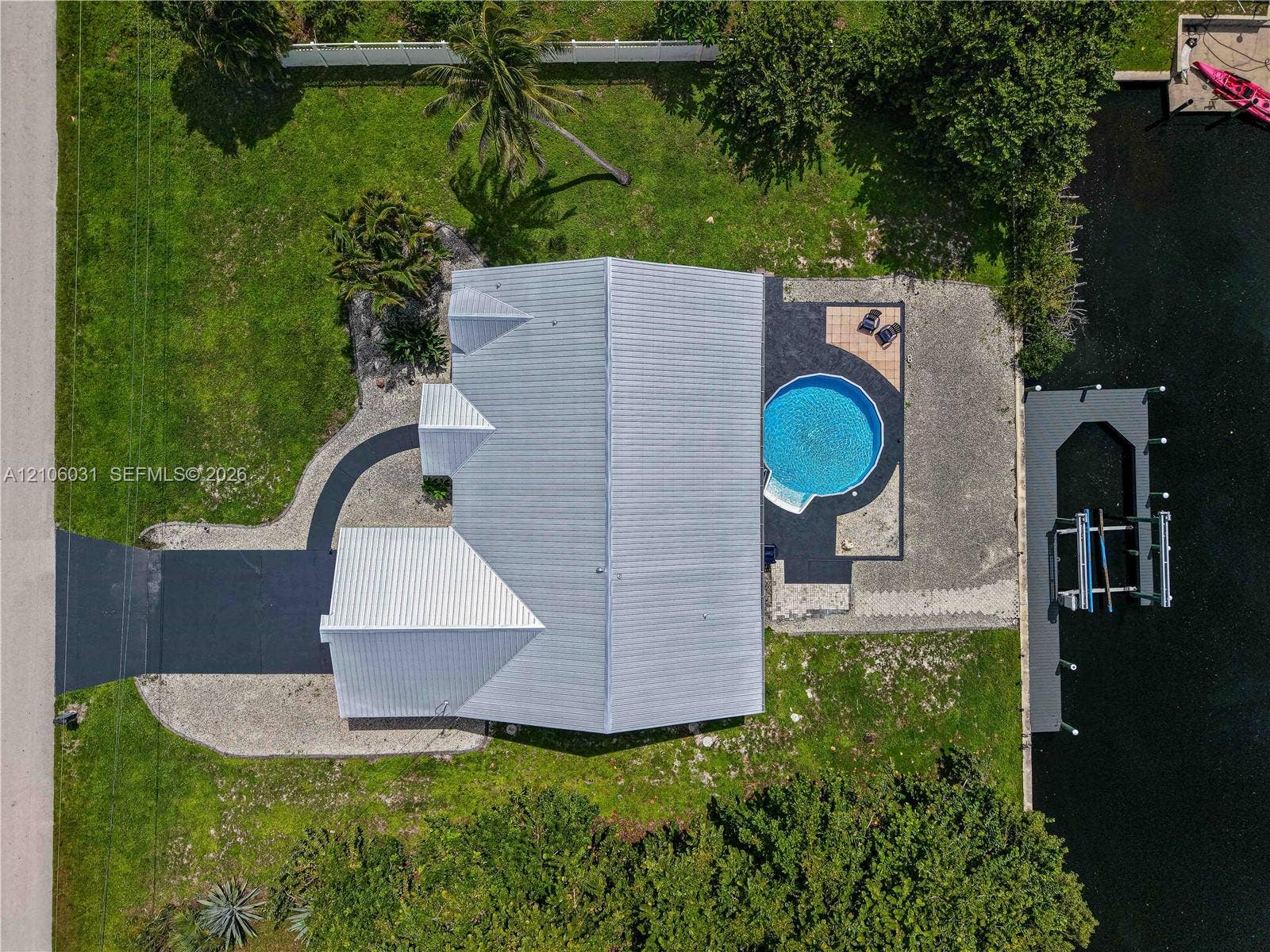 1106 SE 23rd Place, Cape Coral, FL 33990 Waterfront property featuring a metal roof, a private boat dock with lift, an inground circular pool, and paved driveway