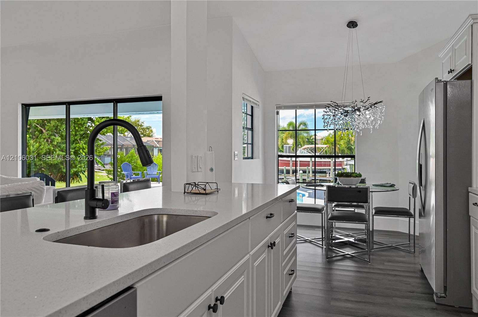 1106 SE 23rd Place, Cape Coral, FL 33990 Kitchen featuring a quartz countertop, stainless steel undermount sink, matte black gooseneck faucet, white shaker-style cabinetry, and wood-finish flooring