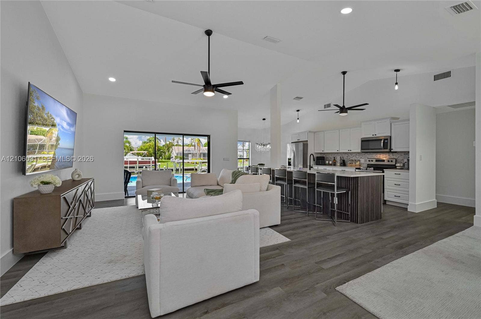1106 SE 23rd Place, Cape Coral, FL 33990 Open-concept interior featuring vaulted ceilings, wood-finish flooring, a kitchen island with cabinetry seating, and large sliding glass doors