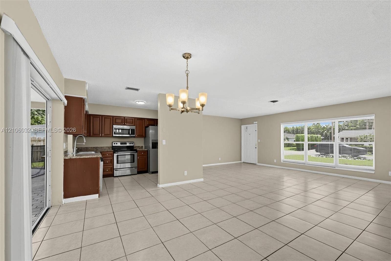 759 NW 7th Street, Boca Raton, FL 33486 Open-concept interior featuring light-toned tile flooring, stainless steel appliances, dark wood cabinetry, a multi-light chandelier, and large windows