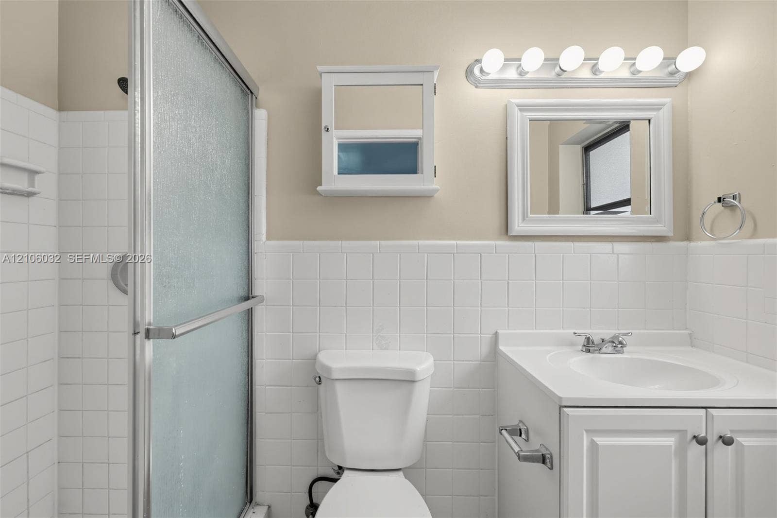 759 NW 7th Street, Boca Raton, FL 33486 Bathroom featuring white square tile wainscoting, shower enclosure with frosted glass panels, white vanity cabinet with a solid-surface top, wall-mounted medicine cabinet, and six-bulb vanity lighting