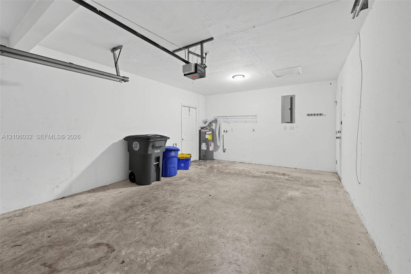 759 NW 7th Street, Boca Raton, FL 33486 Enclosed garage space featuring a concrete floor, painted walls, ceiling-mounted garage door opener, and integrated electrical service panel
