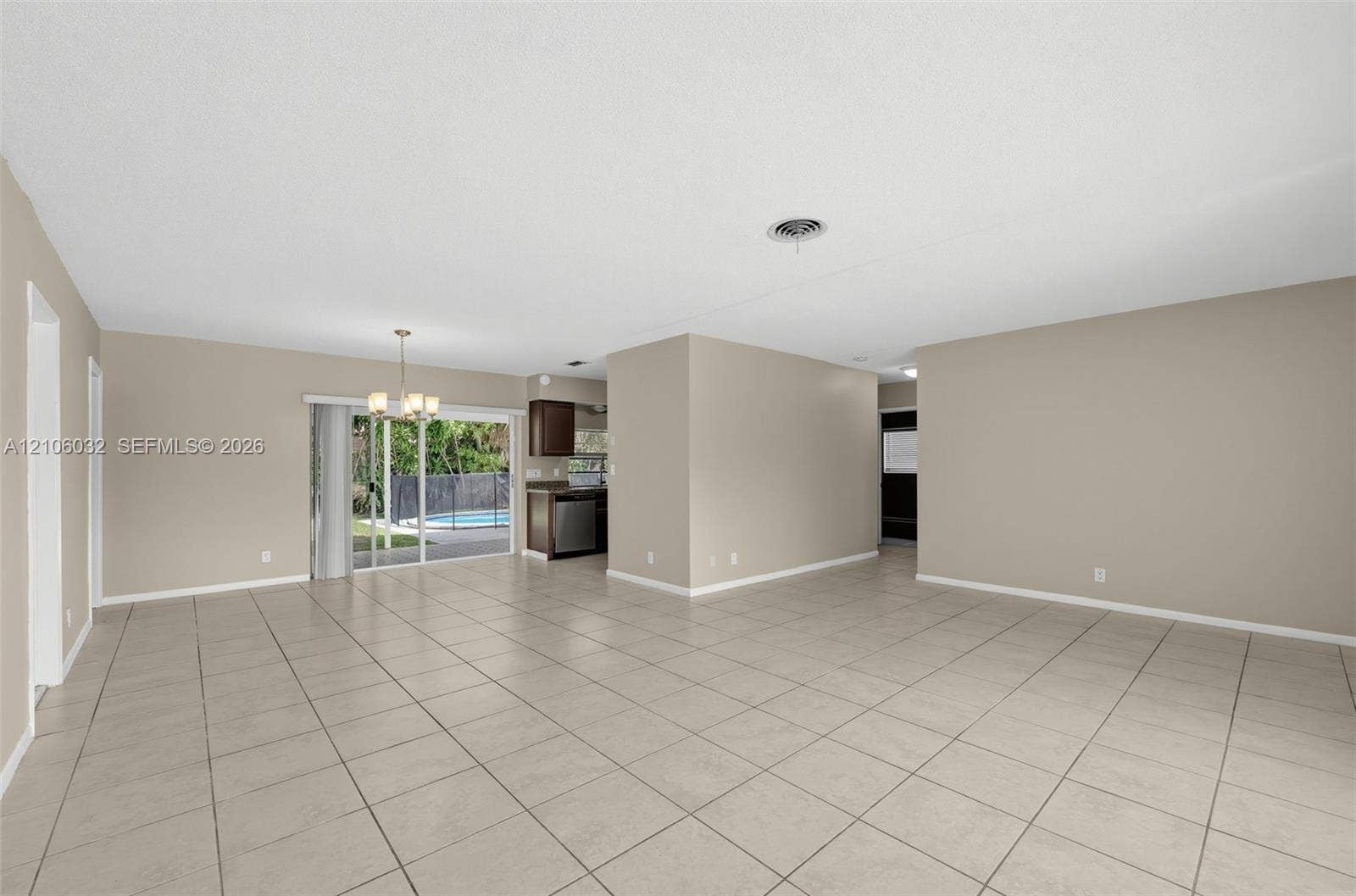 759 NW 7th Street, Boca Raton, FL 33486 Open living area featuring large-format neutral floor tile, sliding glass door access to a screened-in pool, and a dedicated dining space with a hanging chandelier